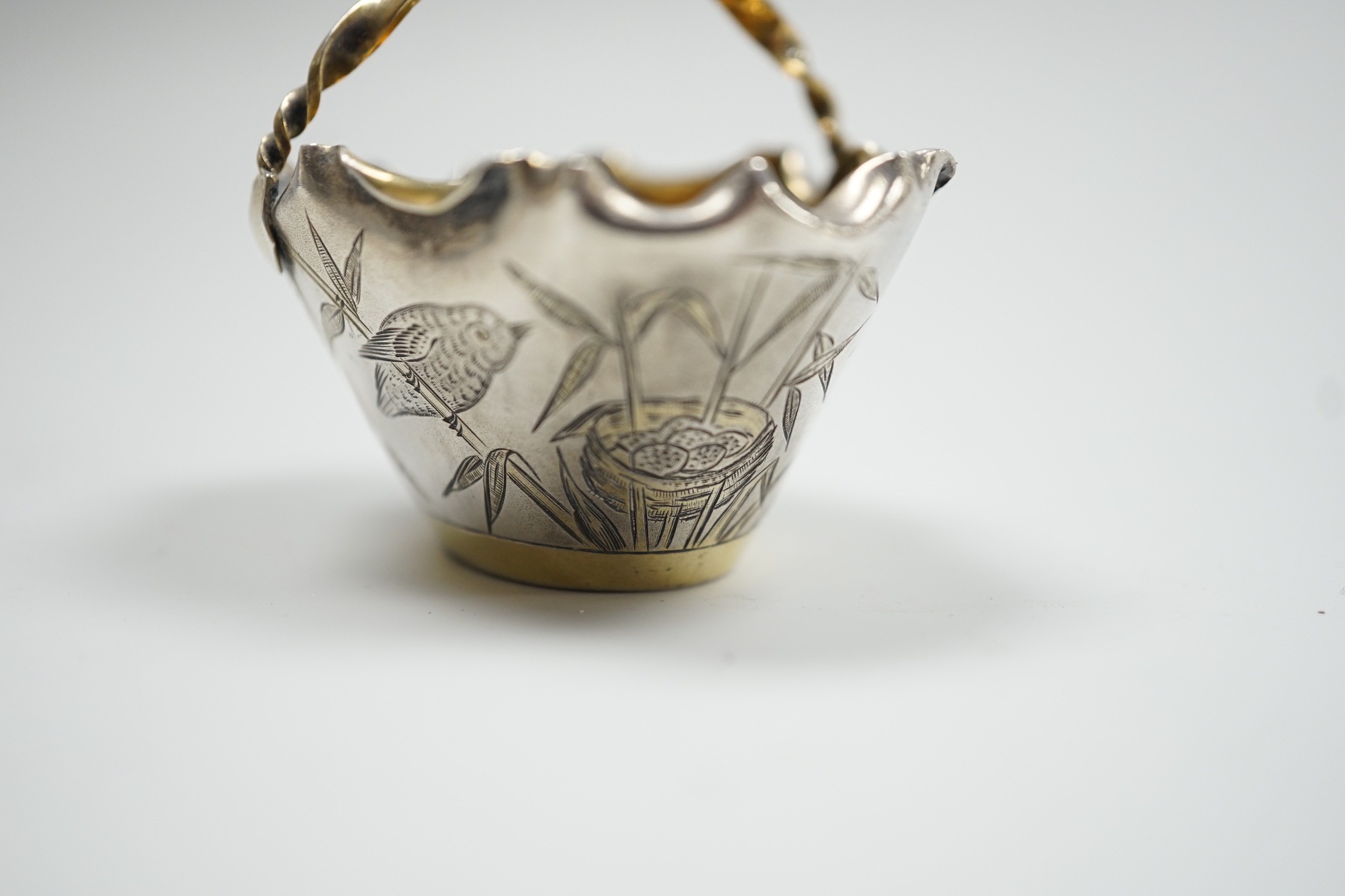 A late Victorian novelty parcel gilt silver salt modelled as a basket, with aesthetic engraved decoration, London, 1884, length 65mm, together with an Egyptian white metal small dish.